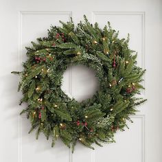 a wreath hanging on the front door with lights and greenery around it's edges