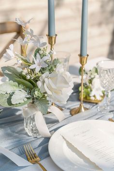 the table is set with white flowers and gold place settings for an elegant dinner party