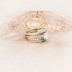 two gold rings with turquoise stones on them sitting on a piece of tree bark in front of a white background