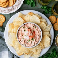 a white plate topped with chips next to a bowl of shrimp dip and crackers