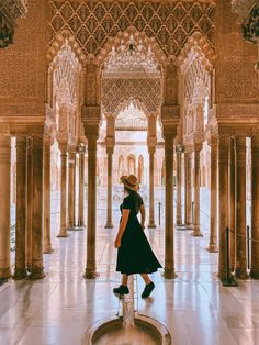 a woman in a black dress and straw hat walking through an ornate building with columns