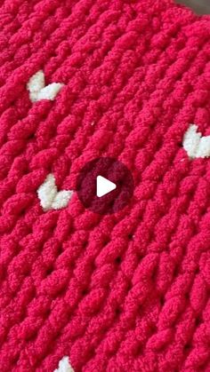 a red crocheted blanket with white hearts on it and a video play button