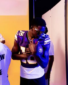 two men standing next to each other in front of a yellow wall wearing football uniforms