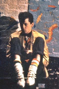 a young man sitting on top of a wooden bench next to a wall covered in graffiti