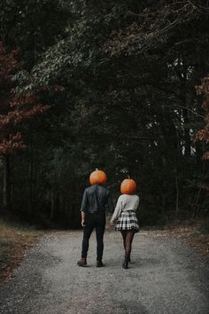 two people walking down a road with pumpkins on their heads and one person holding the other's hand