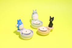 three small candles are sitting in bowls with animals on them and one has a cat figurine next to it