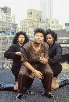 three women are sitting on the ground in front of some buildings and one woman is holding her hand out