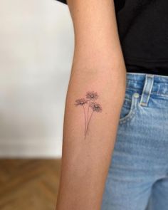 a woman's arm with a small tattoo of three dandelions on it