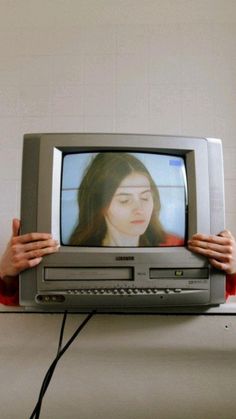 two hands holding up a television with a woman's face on it