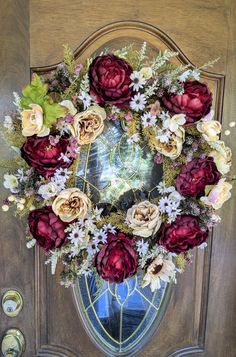 a wreath is hanging on the door with flowers and leaves around it in front of a mirror