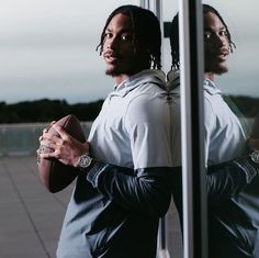 a man standing in front of a window holding a football and looking into the mirror