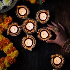 a woman's hands are holding candles in front of flowers on a wooden table