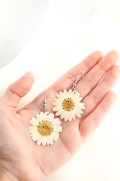 a person is holding two white and yellow flowers in their hand, while wearing earrings