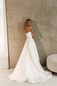 a woman in a white wedding dress leaning against a wall with her back to the camera