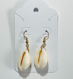 A cowrie shell with either silver or gold earring hook. Gold Teardrop Earrings For The Beach, Cowrie Shell Dangle Jewelry Gift, Cowrie Shell Dangle Jewelry For Gifts, Beach Jewelry For Pierced Ears, Shell-shaped, Gold Cowrie Shell Earrings As Gift, Gold Cowrie Shell Earrings For Gift, Nickel Free Adjustable Shell-shaped Earrings, Nickel-free Adjustable Shell-shaped Earrings, Cowrie Shell Dangle Earrings As Gift