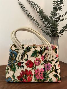 1950s 1960s Garay Floral Needlepoint Tapestry Top Handle Handbag, Vintage Purse, Mid Century Accessory Eye catching Garay floral needlepoint tapestries handbag made in the 1950s 1960s. It features a pretty multi colored needlepoint tapestry floral design on all sides. Double vinyl handle straps. There is gold tone metal hardware with a bright and shiny thumb lift closure that closes with that lovely "snapping" sound letting you know that everything inside is safe and secure. Opens to a fabric lining with one interior area and two separate compartments on either side. The center section has an interior side metal zippered pocket. Attached GARAY label. Protective feet are on the bottom of the bag. Mint condition *the exterior is immaculate.  The lining is immaculate.  The metal hardware is b Rectangular Embroidered Bags For Vintage Events, Embroidered Rectangular Bags For Vintage Events, Embroidered Rectangular Bag For Vintage Events, Vintage Floral Embroidery Bags For Formal Occasions, Vintage Floral Embroidered Bag For Formal Occasions, Retro Embroidered Evening Bags, Elegant Tapestry Bags With Adjustable Handle, Elegant Bag With Top Handle And Floral Embroidery, Vintage Cream Embroidered Bag