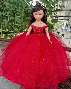 a doll wearing a red dress and tiara standing in front of a fenced area