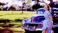 a woman standing in front of an old car