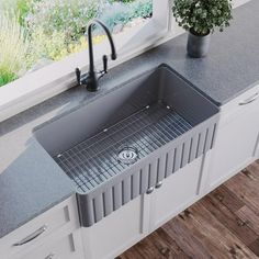 a stainless steel kitchen sink in front of a window with a potted plant on the counter