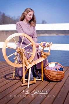 a woman sitting on a wooden deck next to a spinning wheel