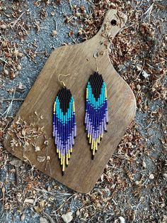 a pair of colorful beaded earrings sitting on top of a piece of wood next to dried leaves