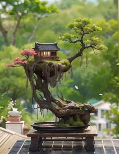 a bonsai tree with a house in the middle and flowers hanging from it's branches