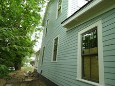 a blue house with white trim on the side and trees in the yard behind it