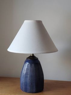 a blue vase sitting on top of a wooden table next to a white lampshade