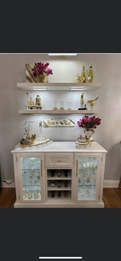 a white and gold bar with wine glasses on it's glass doors, two shelves above the bar