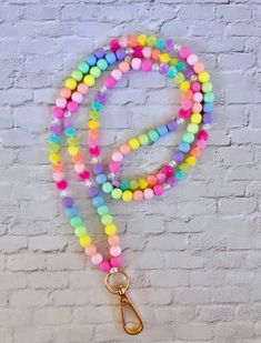 a multicolored beaded lanyard with a gold hook on a white brick wall