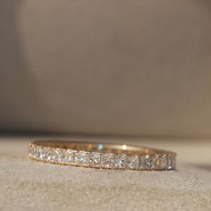 a gold wedding band with five princess cut diamonds on the side, sitting on a beige surface