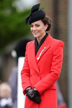 a woman in a red coat and black hat smiles at the camera while wearing gloves