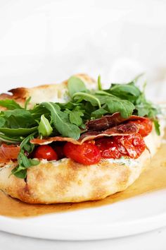 a close up of a pizza on a plate with greens and tomatoes in the middle