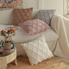 a white couch with pillows on top of it next to a potted plant and vase