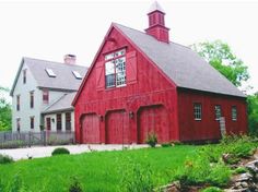 a red barn with a clock tower on the top and green grass in front of it