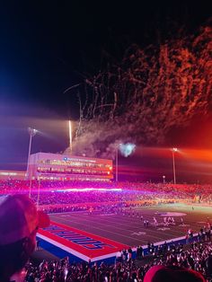 fireworks are lit up in the night sky over a football field as people watch from the stands