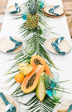 the table is set with plates, fruit and pineapples on top of it