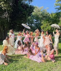 a group of women in dresses and parasols posing for a photo on the grass