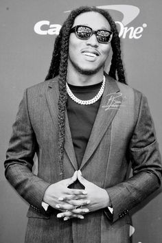 a man with dreadlocks and sunglasses standing in front of a wall wearing a suit