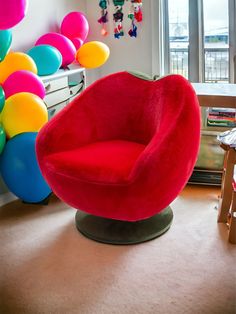 a red chair sitting in the middle of a room with balloons hanging from the ceiling