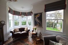 a living room filled with furniture next to two windows and a painting on the wall