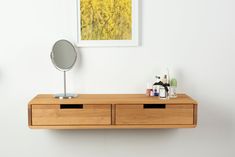 a wooden table with two drawers and a mirror on it next to a wall mounted art piece