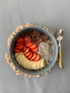 a bowl with bananas, strawberries and granola in it next to a spoon