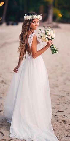 a woman standing on top of a sandy beach wearing a white dress and flowers in her hair