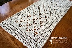 a crocheted table runner sitting on top of a wooden table