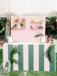 a pink and green striped bar with palm leaves on the table in front of it