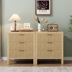 a wooden dresser with flowers and pictures on the wall next to a lamp in a living room