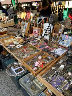 a table filled with lots of assorted items and people looking at them in the background