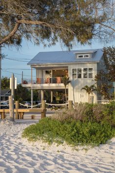 a white house with a blue roof sitting on the beach next to a fence and trees