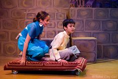 two young children sitting on top of a red rug in front of a stage backdrop